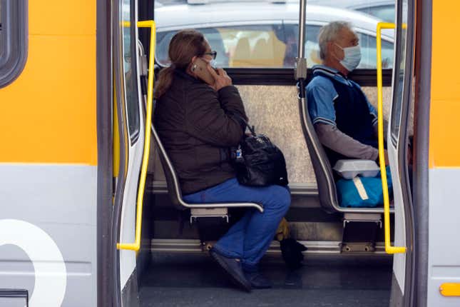 Two people wearing surgical masks sit on a bus in Los Angeles County.
