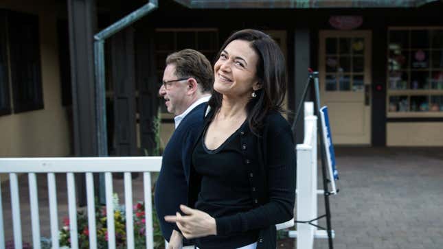 Facebook COO Sheryl Sandberg smiles at the camera while Activision Blizzard CEO Bobby Kotick walks behind her looking at the ground.