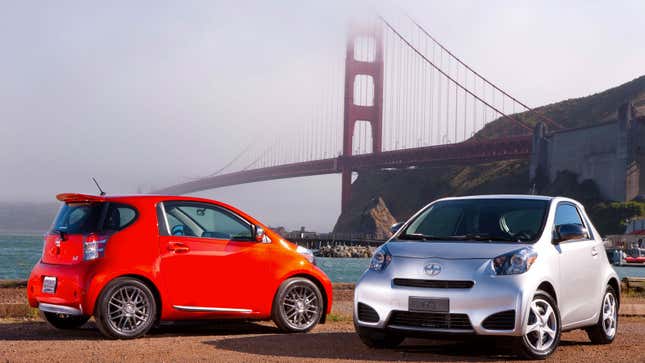 A photo of two Scion IQ city cars parked in front of a bridge. 