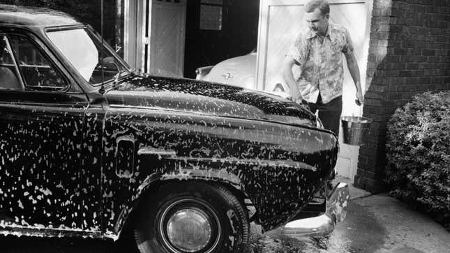 Una fotografía en blanco y negro de un hombre limpiando un coche. 