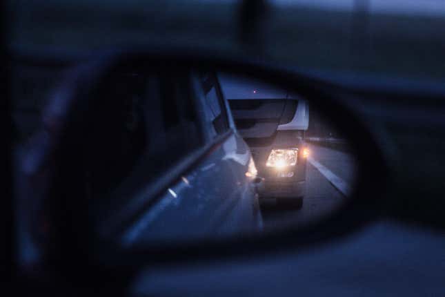 A semi truck is following a car too closely, image seen in car's rear-view mirror