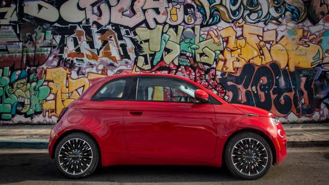 A side view of a red 500e parked in front of a graffiti wall