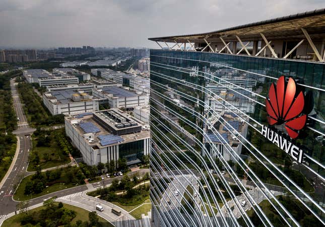 aerial photo of Huawei logo seen on glass building on right of photo, the left shows shorter buildings and a road