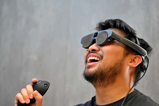 man wearing augmented reality glasses holding a remote looking up smiling