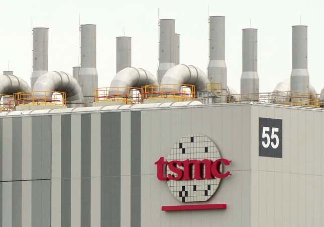 red TSMC letters on a logo designed after a silicon wafer on the side of a building with tubes and pipes at the top