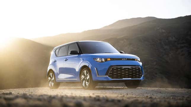 Une Kia Soul bleue garée sur un terrain vague devant un coucher de soleil