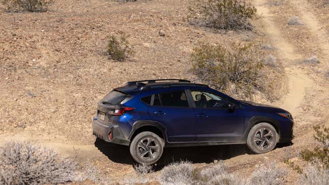 A blue Crosstrek kicking a back wheel up on a dusty off-road trail