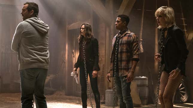 Four people stand with chains around their necks in a barn. 