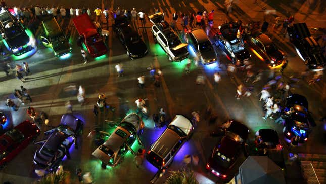 Cars are parked up with neon lights shining from underneath. 