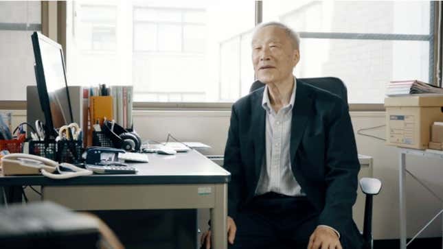 Uemura sits at a desk, smiling at the camera. 