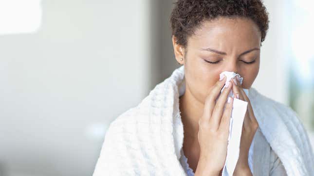 A woman with a white blanket over her shoulders blows her nose.