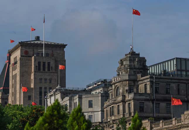 a Chinese worker, top right of photo, raises a new national flag on the top of a building