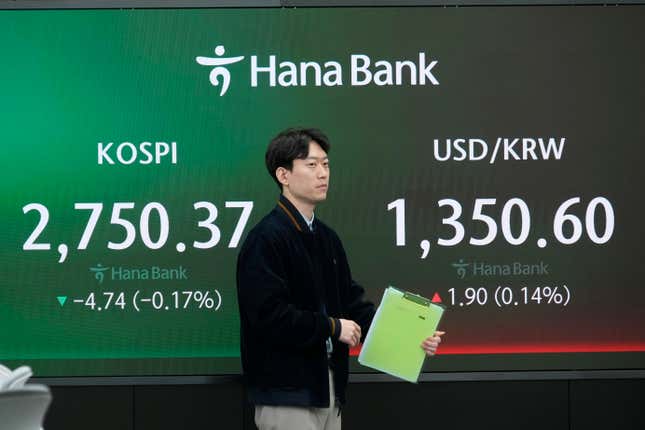 A currency trader moves by the screens showing the Korea Composite Stock Price Index (KOSPI), left, and the foreign exchange rate between U.S. dollar and South Korean won at the foreign exchange dealing room of the KEB Hana Bank headquarters in Seoul, South Korea, Thursday, March 28, 2024. Asian shares were mixed on Thursday after U.S. stocks broke out of a three-day lull to close at a record.(AP Photo/Ahn Young-joon)