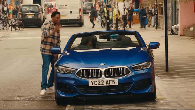 A vibrant blue BMW on a London city street, with a Black woman in the passenger seat and a man standing next to it. 