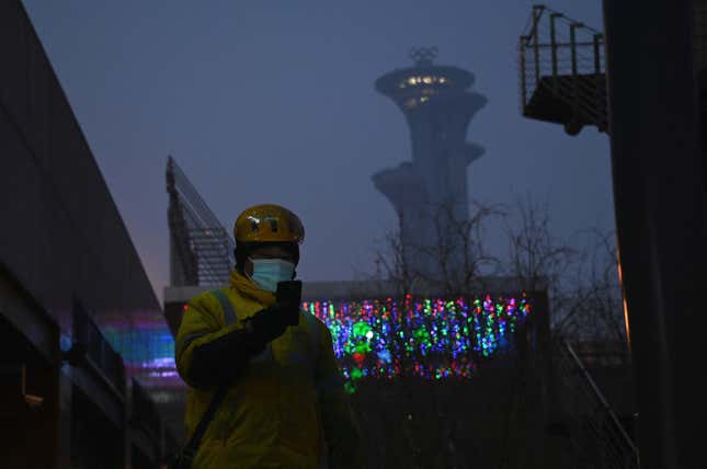 A delivery worker uses a mobile phone as the Beijing Olympic Tower is seen during a smoggy day in Beijing on January 24, 2022. 