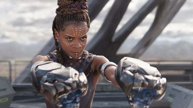 Letitia Wright in action as Shuri in Black Panther, raising two panther-shaped gauntlets up to fire.