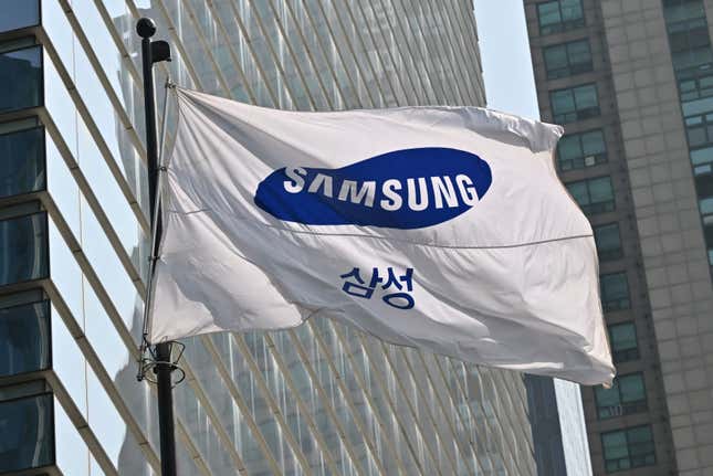 a white flag with samsung logo in english and korean fluttering in the wind in front of grey buildings