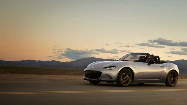 A gray Mazda Miata driving in front of a sunset