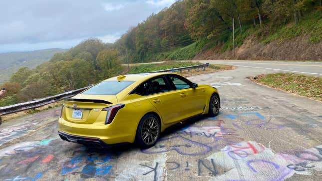 a rear 3/4 shot of the yellow CT5V blackwing on the graffitied pavement in front of trees