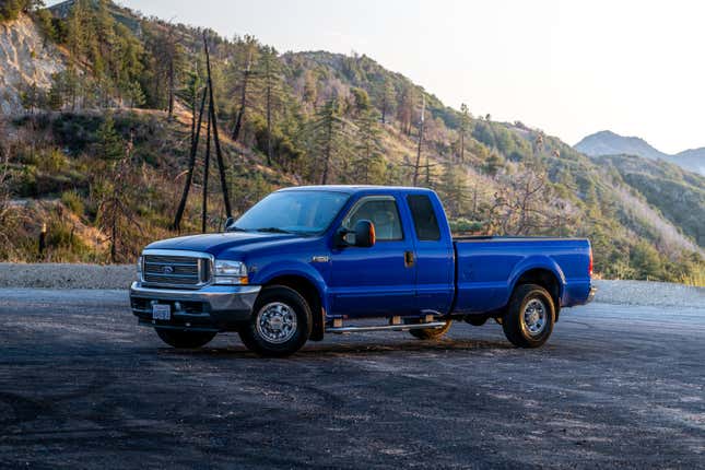 A blue truck parked on pavement in the mountains during magic hour.