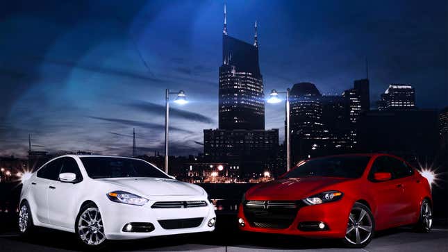 A photo of two Dodge Dart sedans parked in front of a city skyline. 