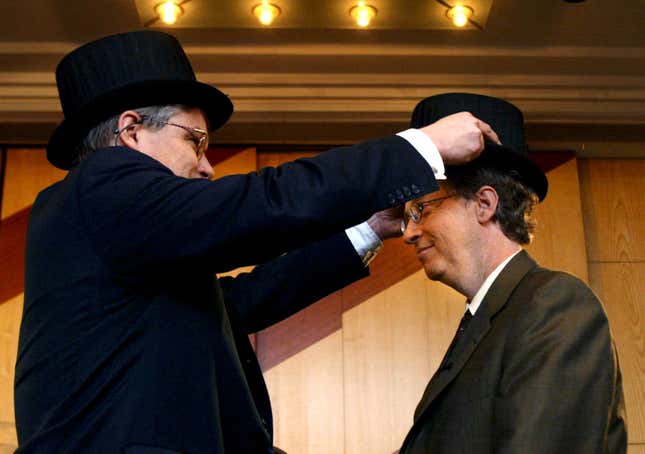 Bill Gates having a doctors hat put on his head by another man in a hat