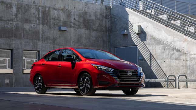 A red Nissan Versa parked in front of concrete structures