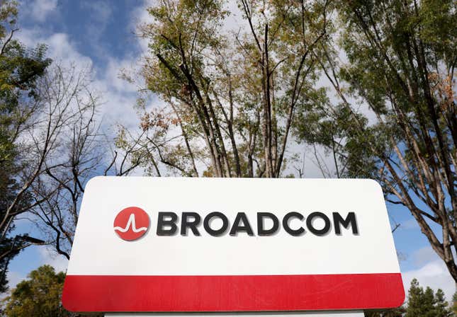 upward view of broadcom logo and name on a white and red sign in front of trees and a cloudy blue sky