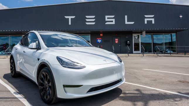 A photo of a white Tesla Model Y SUV outside a factory. 