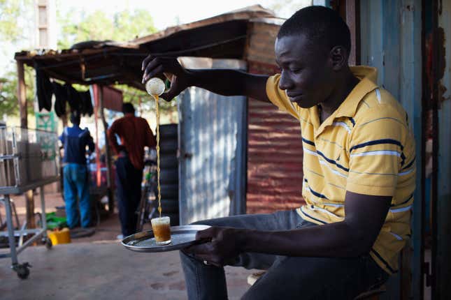 A street vendor prepares tea in Bamako, Mali, foaming the top by pouring it between cups.