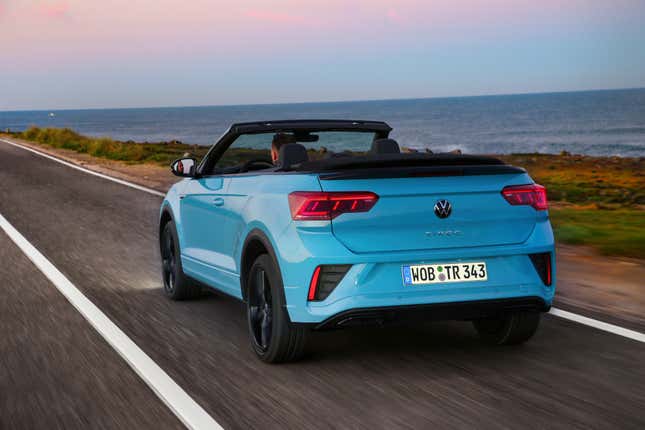 rear 3/4 view of a blue Volkswagen T-Roc Convertible driving along the coast