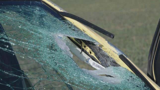 A hole created by a rock in the windshield of a yellow car.