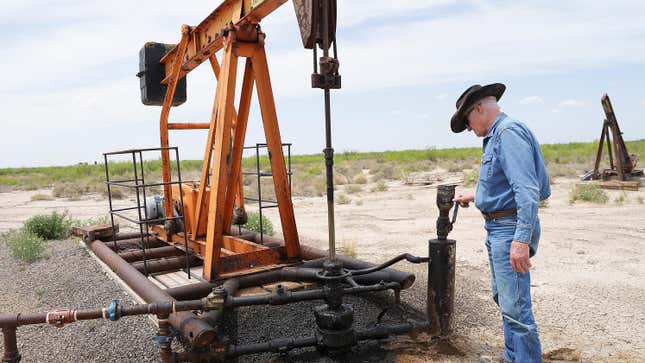 A rancher in a cowboy hat looks at a leaky oil pump jack.