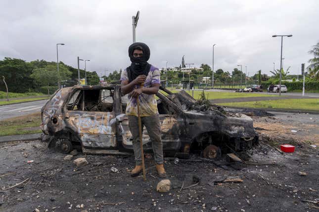 A man in New Caledonia stands in front of a burned out car on May 14, 2024. 