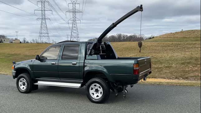 a dark green Toyota Hilux with the crane extended parked in front of grassy hills and powerlines