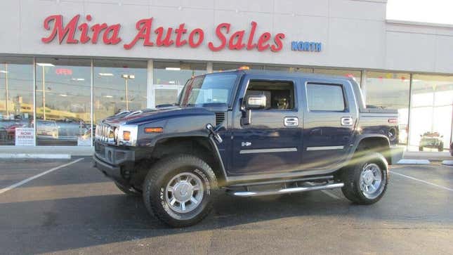 A side view of a Hummer H2 SUT parked in front of a car showroom