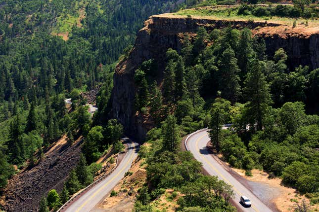 aerial view of the serpentine bend in the Historic Columbia River Highway with lush green trees and a lone car on the road