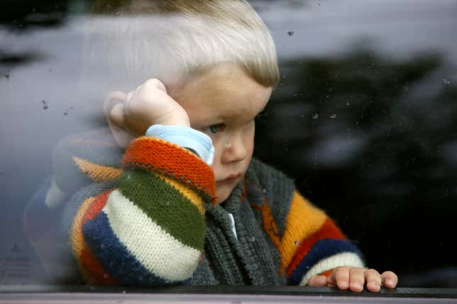 Blonde boy in striped sweater stares out of window dolefully.