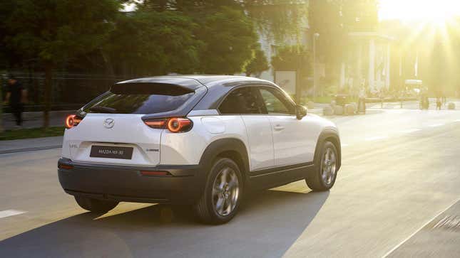 Rear-quarter view of a white European model Mazda MX-30 driving down a city street.