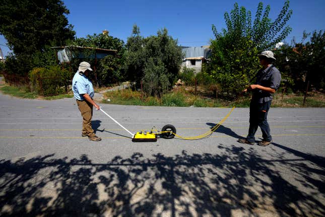 Harry M. Jol, left, a geography and anthropology professor at the University of Wisconsin Eau Claire, and his son Connor, right, operate a ground-penetrating radar in the village of Exo Metochi, Duzova, in the Turkish occupied area at breakaway Turkish Cypriot north of ethnically divided Cyprus on Tuesday, Sept. 5, 2023. Emitting radio waves, the machine is probing for any disturbances through layers of soil beneath the asphalt to offer any clues supporting eyewitness accounts that people who vanished nearly a half century ago are buried in a makeshift mass grave, now squeezed between a two-story home and a fig orchard. (AP Photo/Petros Karadjias)