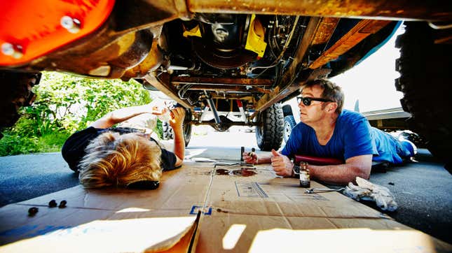 Father and son lying on driveway under off road vehicle replacing oil pan gasket