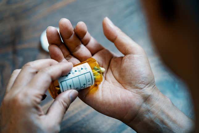 Close-up of a male hand holding a pill bottle and pouring medication into his hand in his house