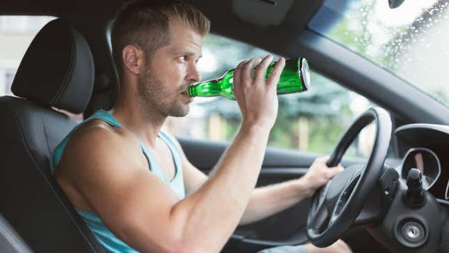 Drunk driver drinking behind the steering wheel of a car