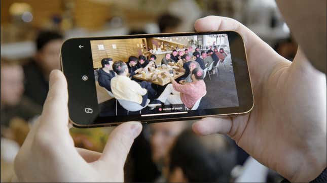 hands holding a phone using Molmo, the camera is being used to see people sitting at a long table with digital markers on their heads