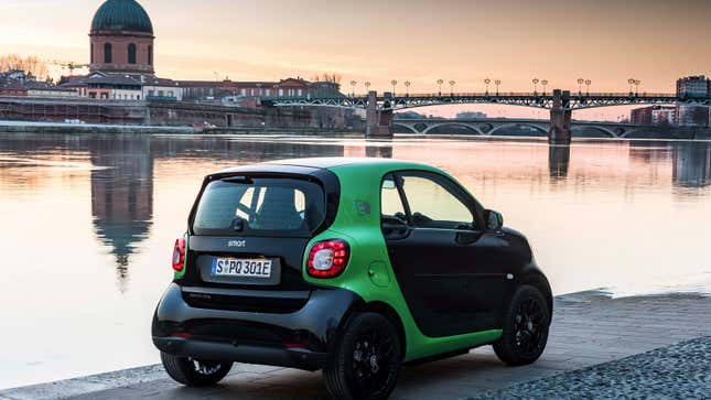 A photo of a black and green Smart ForTwo city car parked near a river. 