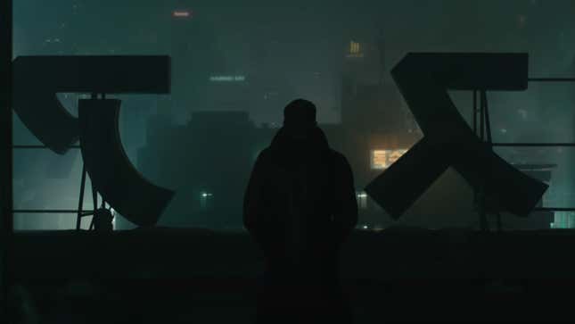 K, the Blade Runner, stands silhouetted against the city he's looking down on from a tall building.
