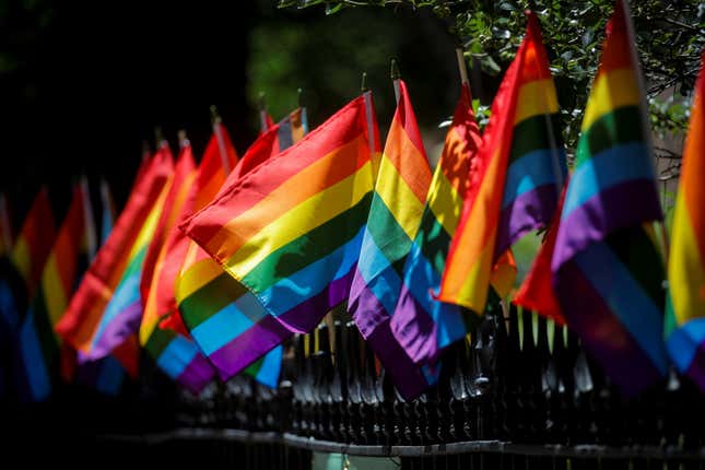 A line of pride flags attached to the top of a wrought iron fence.