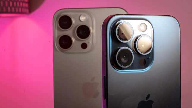 An iPhone 15 Pro next to an iPhone 15 Pro Max showing their camera arrays against a pink background.