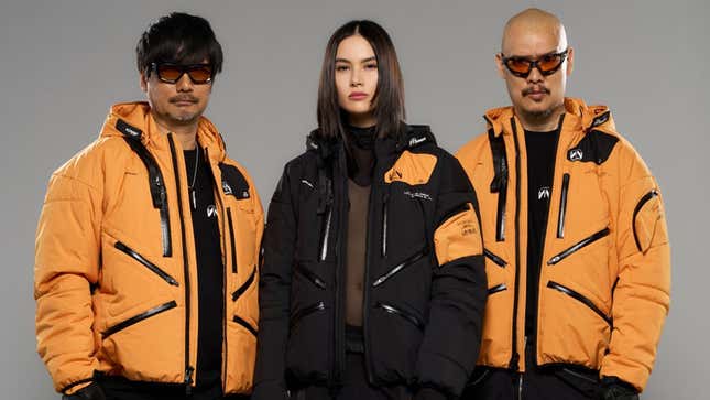 Three models stand wearing the Acronym x Kojima Productions jacket.