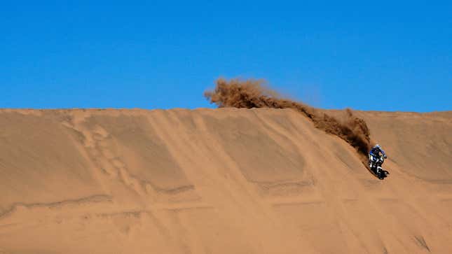 A photo of a motorbike racing down a sand dune. 